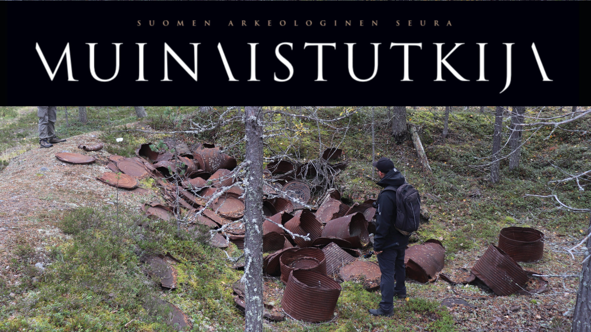 Man at Kemijärvi forested airfield observing abandoned and rusted barrels for calcium chloride made by Solvay in Belgium.