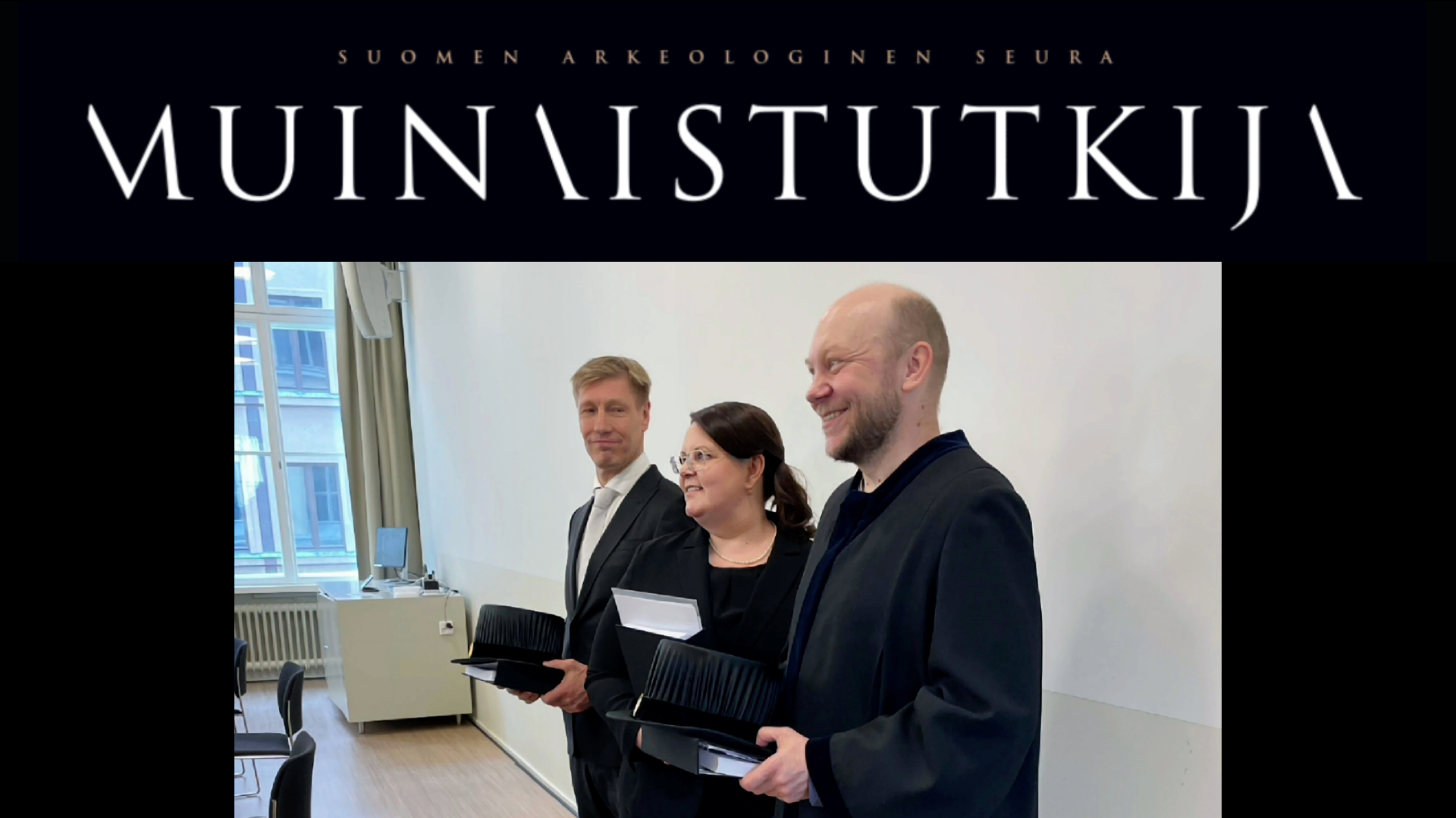 Kuva väitöstilaisuudesta: Kustos ja vastaväittäjä seisovat hatut kädessä väittelijän molemmin puolin.